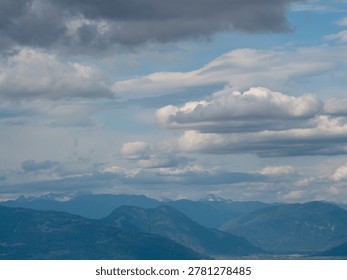 Dramatic layered clouds drift above a blue sky and distant mountain range in British Columbia, Canada.