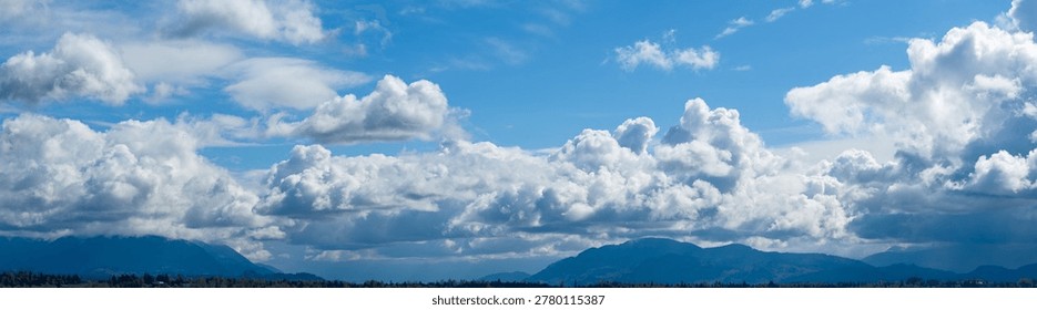 Dramatic layered clouds roll over distant mountain peaks under bright blue sky, a cloudscape in British Columbia, Canada.
