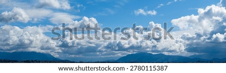 Dramatic layered clouds roll over distant mountain peaks under bright blue sky, a cloudscape in British Columbia, Canada.