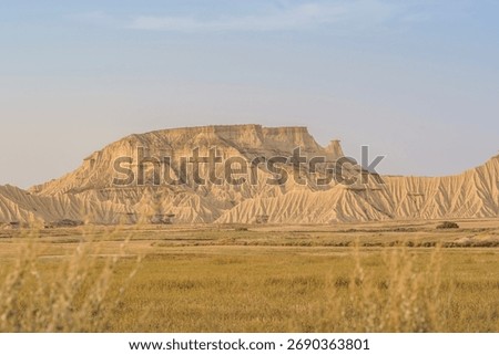 Dramatic layered mesa with deeply eroded cliffs viewed through agricultural field in Bardenas Reales, Navarra, Spain. Geological badlands landscape for travel