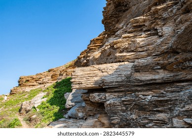 Dramatic layered rock formations on Dongshan Island, Zhangzhou, China. Stratified coastal cliffs showing erosion patterns and geomorphological features with clear blue sky.