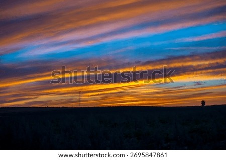 A dramatic, layered sunset sky with striking horizontal streaks of vibrant orange, gold, and deep blue clouds over a dark, silhouetted horizon.