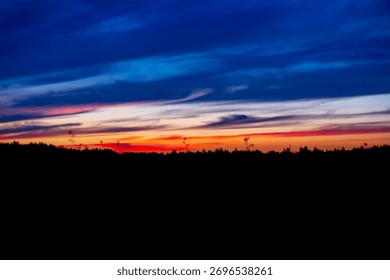 A Dramatic Layered Sunset Sky Transitioning from Fiery Orange and Red to Deep Blue and Purple Over a Dark Forest Silhouette.