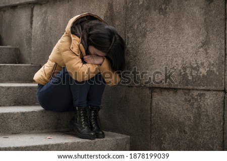 dramatic lifestyle portrait of young attractive sad and depressed Korean woman in winter jacket sitting outdoors on street corner staircase suffering depression problem feeling helpless
