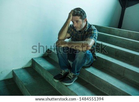 dramatic lifestyle portrait of young depressed and sad man sitting alone outdoors on dark street staircase suffering depression problem and anxiety crisis crying desperate feeling miserable
