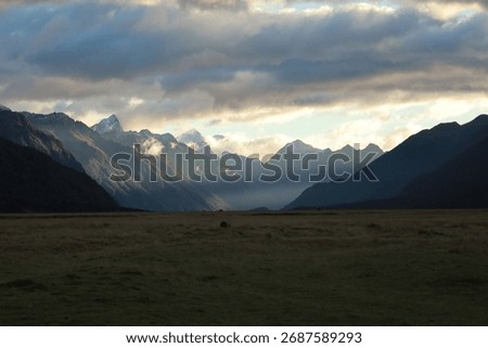 Dramatic light pierces through clouds, illuminating snow-capped mountains above golden plains near Mount Sunday, Canterbury Plains, New Zealand, on May 18, 2025. A majestic Lord of the Rings landscape