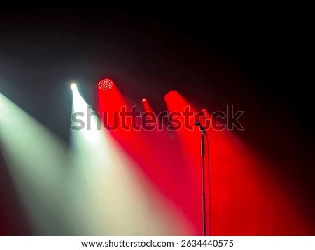 Dramatic lighting illuminates microphone on stage stand with vibrant red and white beams, creating powerful atmosphere for live music, performances, stand-up comedy, and speaking events