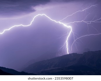 Dramatic lightning bolt over mountain range against rainy night sky