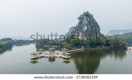 Dramatic limestone karst peak rising from tranquil lake waters with traditional Chinese pavilions on floating platforms at Zhaoqing Seven Star Crags scenic area, China.