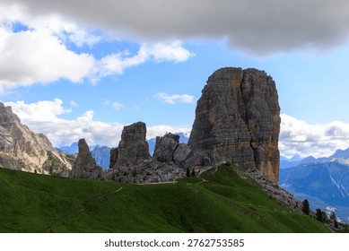 Dramatic limestone rock formations in the Dolomites with green alpine meadows under a cloudy sky, scenic mountain landscape in northern Italy.