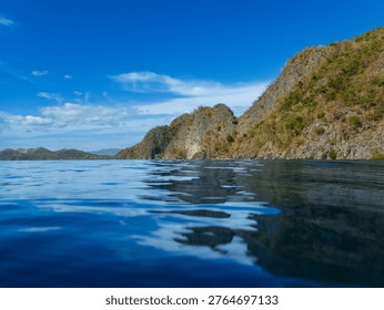 Dramatic limestone rock formations rise from the tranquil blue ocean under a vast sunny sky in the Philippines.