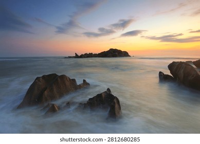 Dramatic long exposure seascape at sunset with
silky smooth ocean waves flowing around large
rock formations. Golden and blue sky reflecting
on calm water. Coastal landscape, nature
background, travel destination.