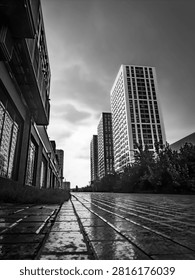 Dramatic low angle shot of high-rise apartment buildings on a wet city street in black and white, featuring strong geometric lines and reflections.