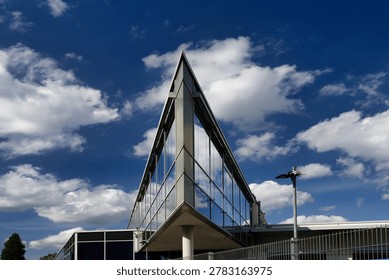 Dramatic low angle shot of a modern glass building with a sharp triangular facade against a blue sky with white clouds in Cologne-Ehrenfeld