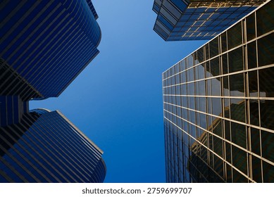 Dramatic low angle upward view of multiple blue glass skyscrapers converging against clear sky
