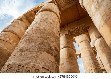 Dramatic low angle upward view of the towering sandstone columns covered in ancient hieroglyphs and colorful relief carvings inside the Great Hypostyle Hall at Karnak Temple, Luxor, Egypt. 