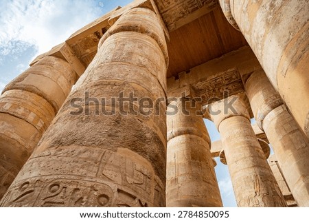 Dramatic low angle upward view of the towering sandstone columns covered in ancient hieroglyphs and colorful relief carvings inside the Great Hypostyle Hall at Karnak Temple, Luxor, Egypt. 