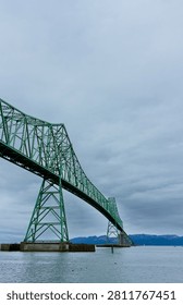 Dramatic low angle view of the green steel framework of the iconic Astoria-Megler Bridge stretching across the wide Columbia River under a moody, overcast sky in Astoria, Oregon.