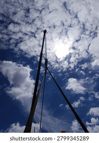 Dramatic low angle view of mobile crane hook block and heavy-duty lifting slings silhouetted against vibrant blue sky with bright sun and clouds. Concept for industrial rigging, heavy lifting operations, construction safety, crane operation and infrastructure logistics.