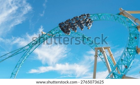 A dramatic low angle view of a roller coaster train navigating a high speed inversion loop against a vibrant blue sky with soft clouds. Riders are suspended upside down capturing excitement motion and adrenaline in a modern amusement park setting. Ideal for themes of thrill adventure entertainment and leisure activities.