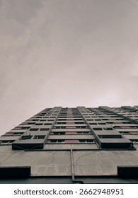 A dramatic low angle view of a tall apartment building reaching into a moody, overcast sky capturing urban minimalism and vertical symmetry
