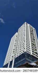 Dramatic low angle view of twin white residential skyscraper towers converging toward a deep blue sky, showcasing modern high-rise architecture