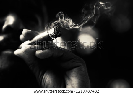 Dramatic low key portrait of a man with beard smoking cigar.The monochrome of a man smoking in dark shade with bokeh. Film stock color tone with grain.Selective focus 