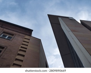 A dramatic low-angle abstract shot looking up at the sharp stone corners and facades of modern and classical buildings against an overcast grey sky.