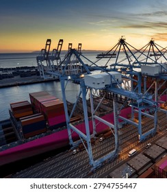 A dramatic low-angle aerial view showcasing towering port cranes positioned above a massive container ship at a busy maritime terminal. The scene highlights global trade, logistics, cargo transportation, and modern shipping infrastructure, emphasizing the scale and efficiency of international supply chain operations.