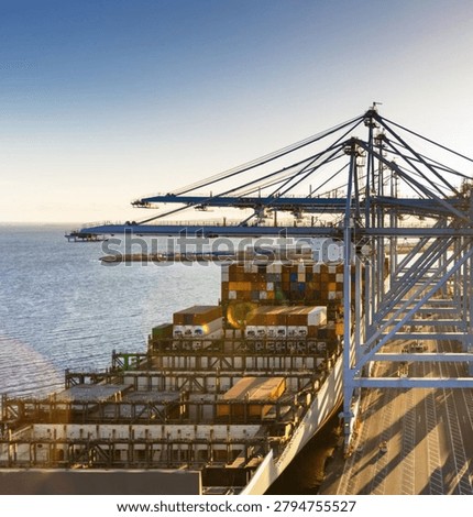 A dramatic low-angle aerial view showcasing towering port cranes positioned above a massive container ship at a busy maritime terminal. The scene highlights global trade, logistics, cargo transportation, and modern shipping infrastructure, emphasizing the scale and efficiency of international supply chain operations.