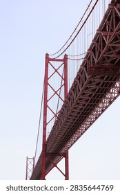 Dramatic low-angle architectural view beneath the 25 de Abril suspension bridge in Lisbon, Portugal, highlighting its massive steel structure and engineering.