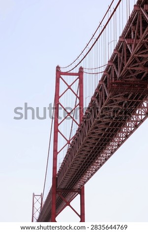 Dramatic low-angle architectural view beneath the 25 de Abril suspension bridge in Lisbon, Portugal, highlighting its massive steel structure and engineering.