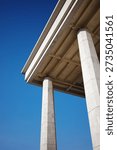 A dramatic low-angle perspective of the iconic National Assembly Building in Yeouido, Seoul, South Korea. The image focuses on the massive granite columns and the intricate underside of the roof structure, set against a crisp, clear blue sky. These pillars, representing the diverse opinions of the people coming together, are captured with sharp detail, highlighting the texture of the stone and the clean lines of Korean monumental architecture. The composition emphasizes strength, transparency, and the solid foundation of democracy. This high-quality photograph is ideal for content related to Korean politics, government administration, Asian landmarks, and civic pride. The bright, natural lighting and minimalist color palette of grey stone and deep blue sky make it a versatile asset for editorial use, educational materials, or travel guides focusing on Seoul