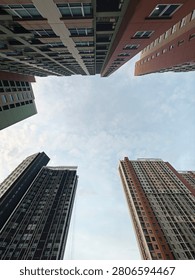 A dramatic low-angle perspective looking up at the towering, modern facades of residential buildings, showcasing the geometric contrast between the warm-toned and cool-toned architecture against the sky.
​A symmetrical, full-frame shot of a towering high-rise apartment building, highlighting the repetitive pattern of balconies and windows reaching toward the sky.
​A wide-angle, low-perspective view capturing multiple high-rise structures converging toward the center of the frame, emphasizing the density and scale of modern urban living.
