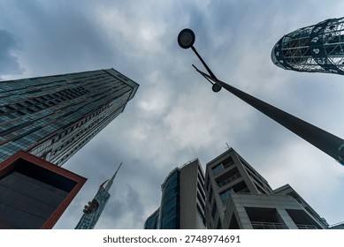Dramatic low-angle perspective of modern skyscrapers in Batumi, Georgia, with a street lamp in the center and stormy clouds above, highlighting the city’s contemporary architecture and urban skyline.

