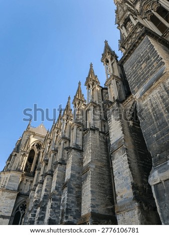 A dramatic low-angle perspective showing the flying buttresses and stone pinnacles of Notre-Dame de Reims. This architectural detail highlights the structural genius of medieval cathedral building.