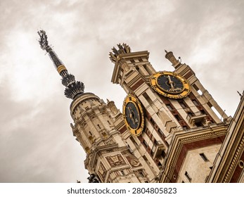 A dramatic low-angle shot of the iconic Moscow State University main building featuring golden clock faces and a towering spire against a cloudy sky, showcasing grand Stalinist architecture.