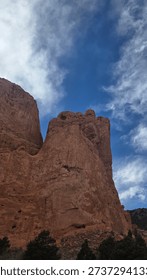 A dramatic low-angle shot of massive red sandstone rock formations reaching toward a deep blue sky with wispy white clouds at Garden of the Gods Park.