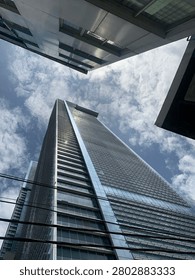 A dramatic low-angle shot of a modern glass skyscraper reaching towards a cloudy blue sky, framed by surrounding urban structures