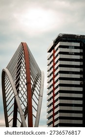 Dramatic low-angle view of contemporary skyscrapers with striking geometric lines and a sculptural curved facade against a cloudy sky. Contrasting materials and converging perspectives create a bold urban composition that conveys innovation, growth, and modern city life.