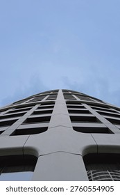 Dramatic low-angle view of cylindrical skyscraper with geometric facade pattern against blue sky
