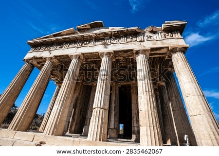 Dramatic low-angle view of the Doric columns, entablature and sculpted frieze of the Temple of Hephaestus in the Ancient Agora of Athens, Greece, against a deep blue sky.