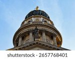 Dramatic low-angle view of the grand dome of the Berlin Cathedral (Berliner Dom) in Germany, showcasing its classical columns, ornate details, gleaming golden statue at its apex against clear blue sky