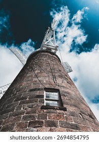 Dramatic low-angle view of a historic stone windmill tower against a dark, stormy, and cloudy blue sky.