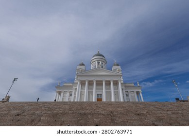dramatic low-angle view of the iconic Helsinki Cathedral Helsingin tuomiokirkko rising above the massive stone steps of Senate Square. A few people are scattered across the stairs beneath a striking