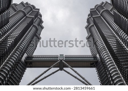 Dramatic low-angle view of the iconic Petronas Twin Towers and connecting skybridge under an overcast sky in Kuala Lumpur, Malaysia.