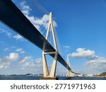 Dramatic low-angle view of a large cable-stayed bridge spanning across calm blue waters against a bright sky with white clouds in Mokpo, South Korea.