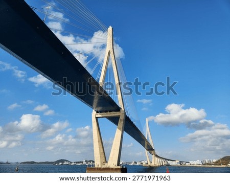 Dramatic low-angle view of a large cable-stayed bridge spanning across calm blue waters against a bright sky with white clouds in Mokpo, South Korea.