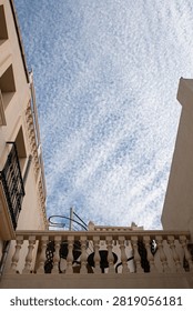 A dramatic low-angle view looking straight up between two buildings in Pego, Spain, framing a striking sky filled with dense altocumulus 