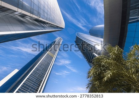 A dramatic low-angle view looking straight up at the modern glass Etihad Towers skyscrapers against a bright blue sky in Abu Dhabi, United Arab Emirates.